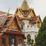 Ornate gilded temple buildings with lush green foliage.